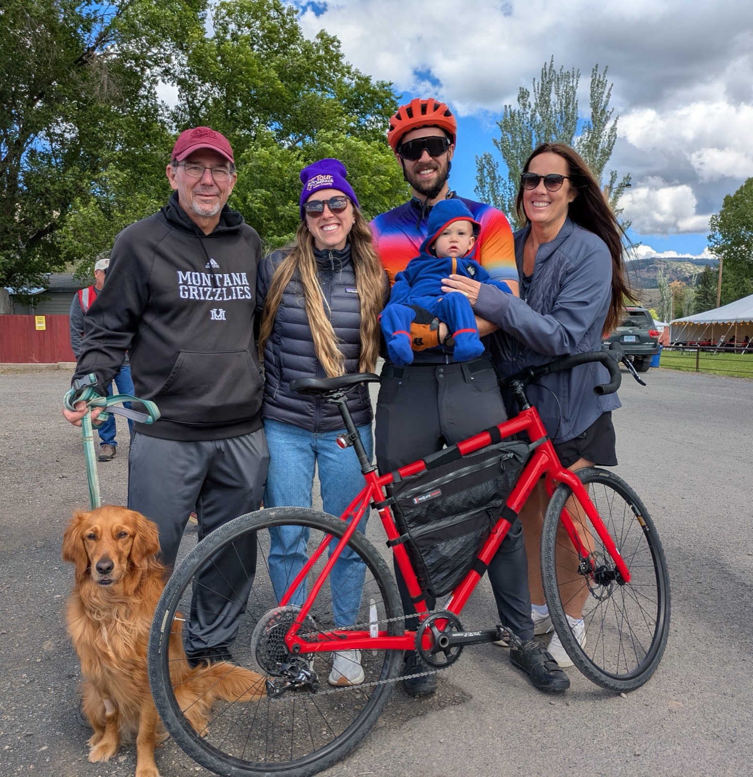 A family and their golden retriever posing with a red gravel bike at the fairgrounds