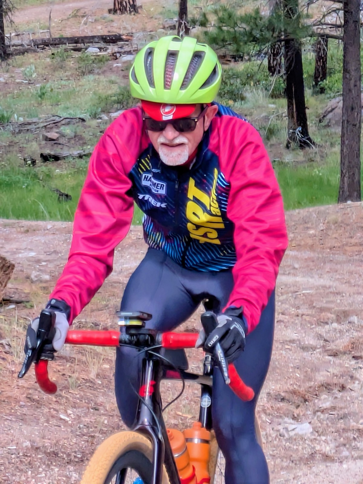 A rider in a bright cycling kit climbing a gravel road through burned pine forest