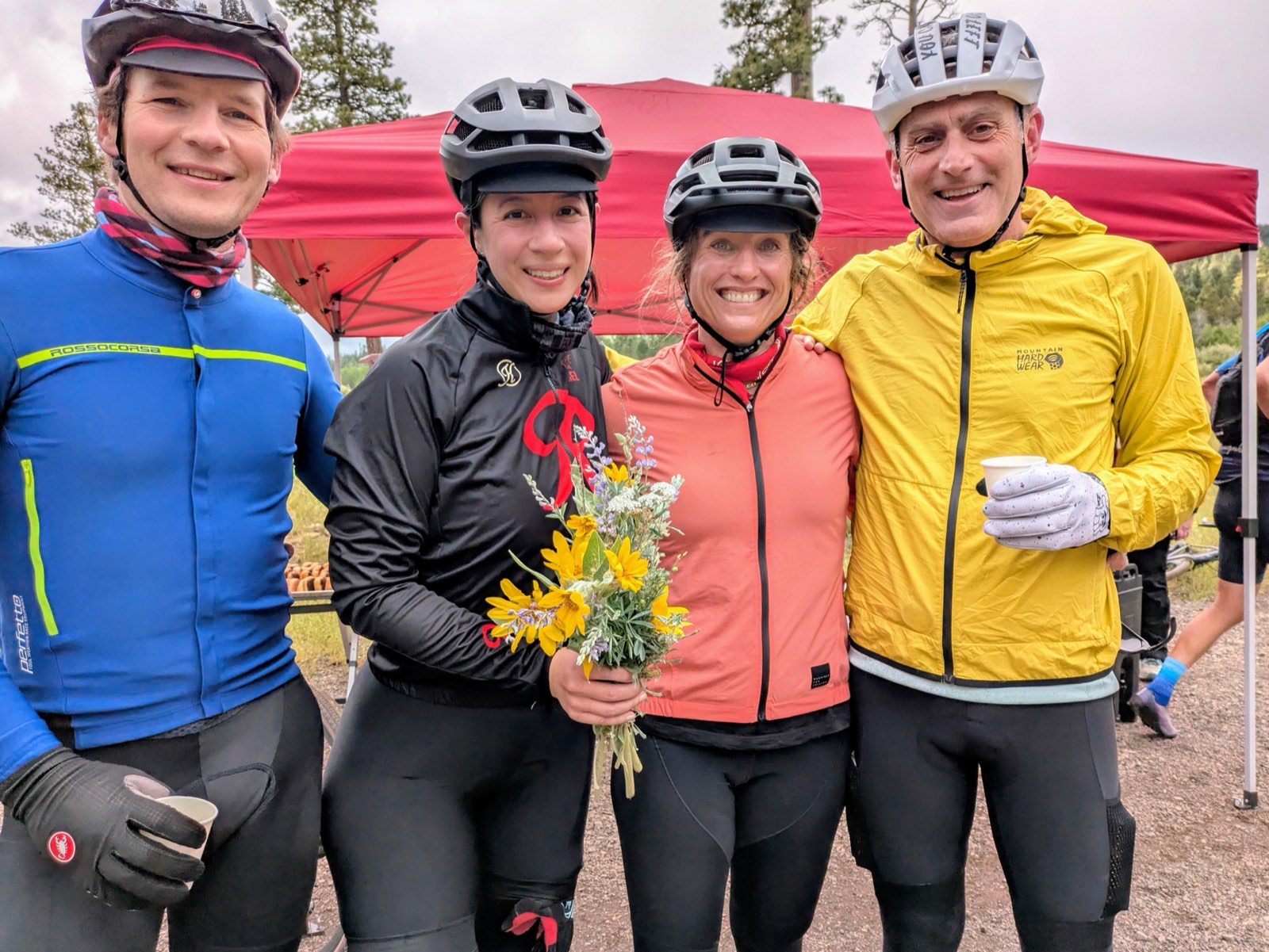 Four riders celebrating at the finish line, one holding a bouquet of wildflowers picked along the route