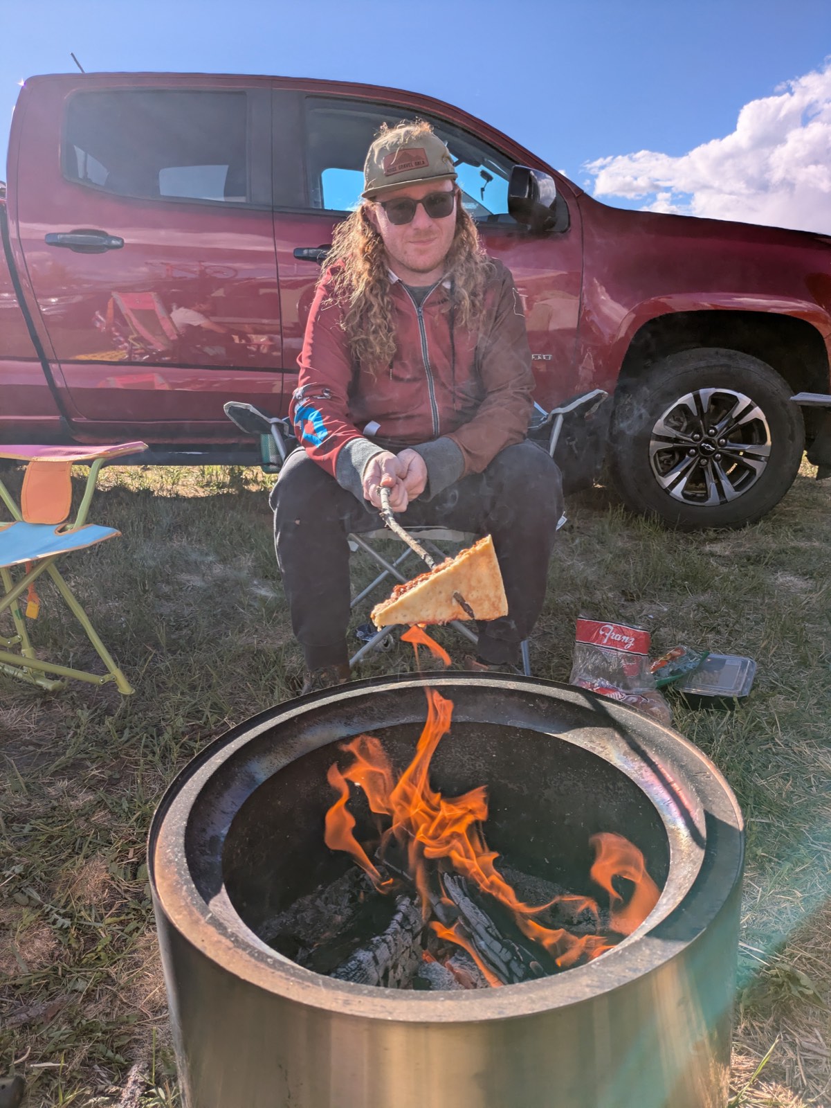 A rider roasting a slice of pizza over a campfire next to his truck at the fairgrounds campground