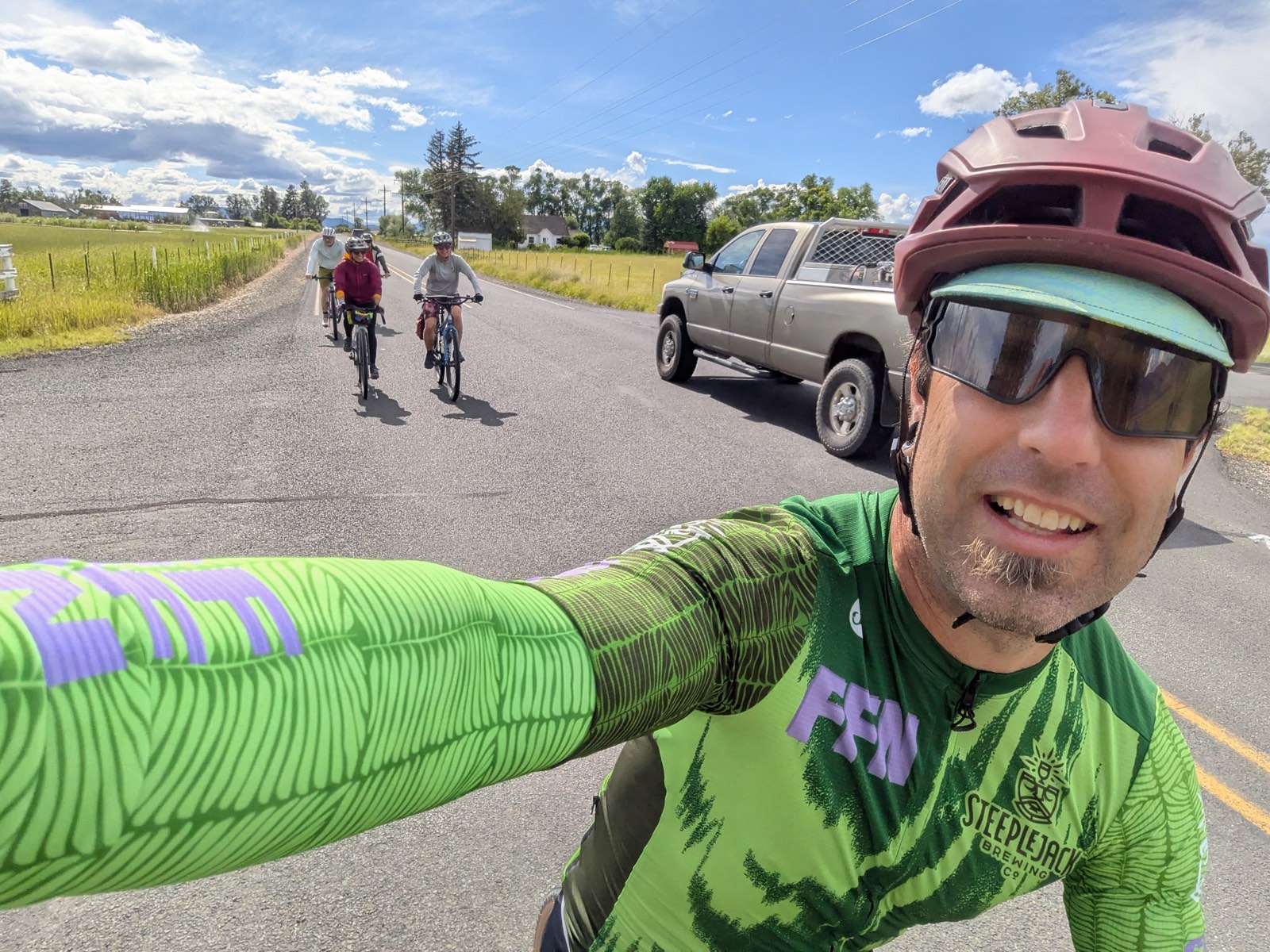 A rider taking a selfie while riding past a farm truck, with the rest of the group following on a country road