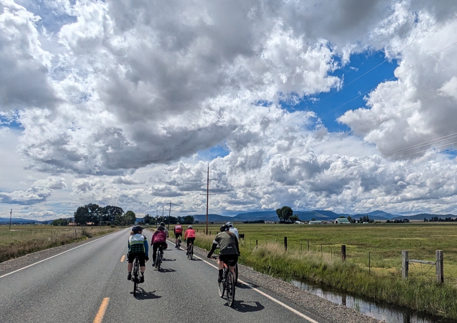 Riders on a farm road beneath a dramatic bank of clouds building over the mountains