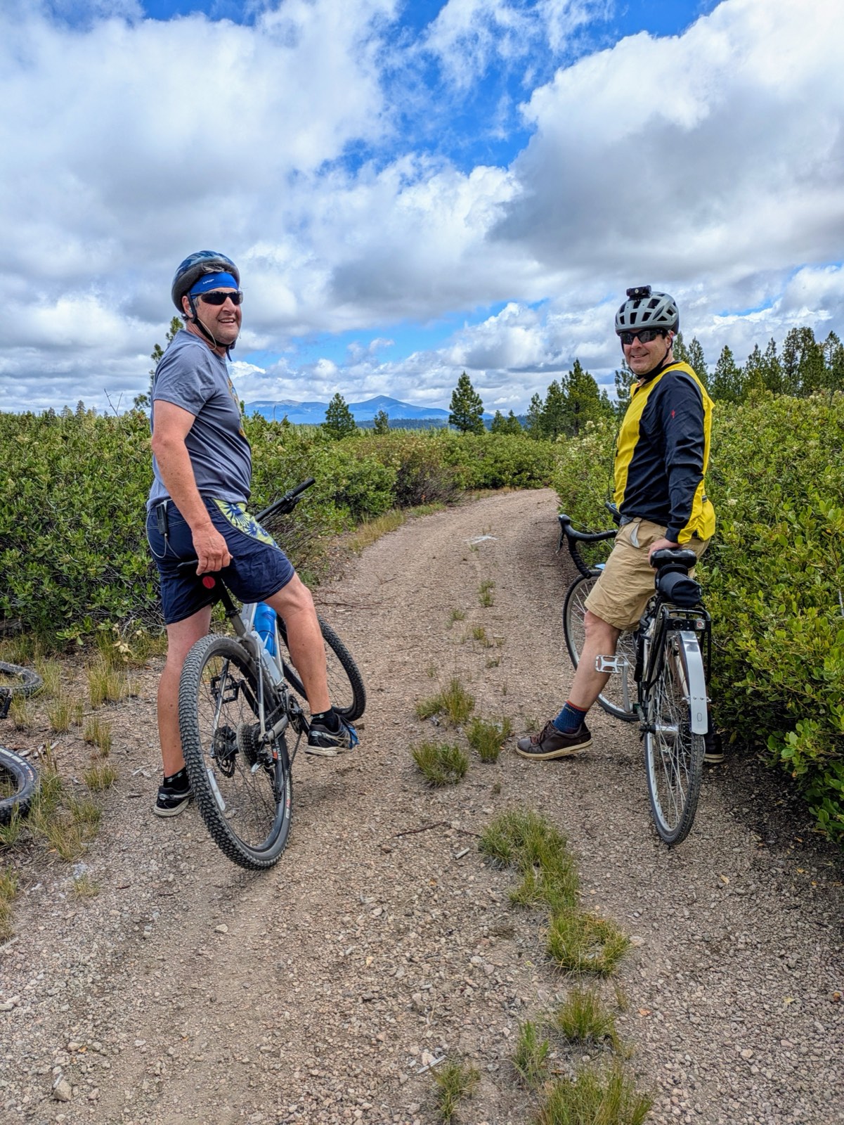 Two riders pausing on a singletrack overlook with mountains in the distance